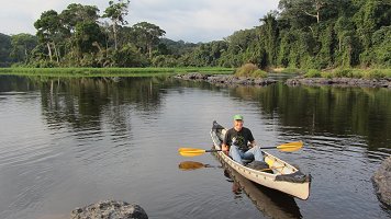 View of Ivindo River showing rocky outcrops and wide mats of semi-aquatic vegetation spreading up to the edge of the dense forest.  John Terborgh is in foreground in canoe showing scale. Click for larger version.
